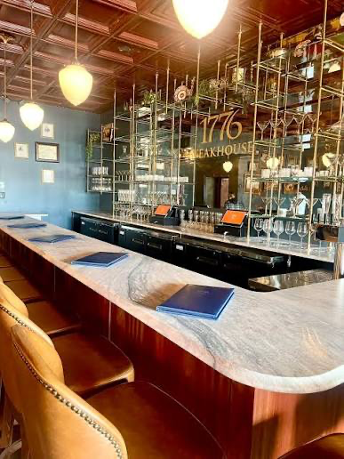 The marble bar counter, leather bar stools and mirrored bottle display at 1776 Steakhouse